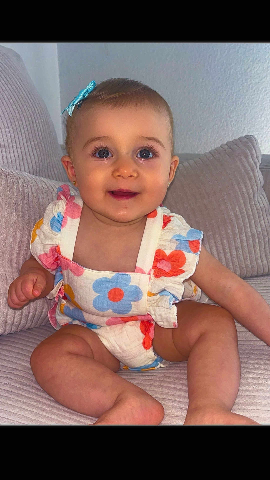 Eyna participe au concours pour gagner de l'argent avec cette photo : baby, child, cute, smiling, blue_bow, floral_outfit, sitting, couch, cozy, indoor, portrait, happy, infant, skin, face, eyes, hand, legs, furniture, home