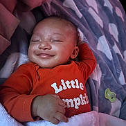 Satori is registered to the contest to win money with this photo: baby, smiling, infant, blanket, orange_clothing, onesie, sleeping, happy, child, cozy, cute, face, hand, pacifier, soft, patterned_blanket, portrait, resting, indoor, toddler