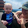 baby, child, woman, holding, outdoor, mountain, scenic_view, building, pagoda, sky, cap, adidas, smile, person, clothing, blue_shirt, green_top, hand, face, nature