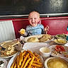 Jason is registered to the contest to win money with this photo: toddler, child, food, meal, fries, mashed_potatoes, gravy, bread, diner, booth, table, plate, smiling, messy_face, indoor, person, clothing, happy, eating, drink