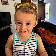 Florina participe au concours pour gagner de l'argent avec cette photo : blanket, bright, casual, child, couch, cute, face, furniture, hair_clips, happy, home, indoor, living_room, person, playful, portrait, smile, striped_shirt, toddler, young_child