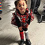 child, clown_costume, face_paint, top_hat, red_flower, black_shoes, colorful_clothing, playful, curious, concrete_floor, stroller, person, pants, sneakers, indoor, costume, festive, fun, small_hat, cute