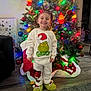 child, toddler, smiling, christmas_tree, christmas_lights, ornaments, holiday, pajamas, grinch, slippers, indoor, festive, decorations, carpet, flooring, home, celebration, joyful, cute, person
