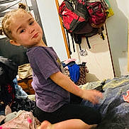 Ava joined the competition — help win amazing prizes! child, curly_hair, purple_shirt, bed, cluttered_room, backpacks, door, clothes, pouty_expression, indoors, furniture, blanket, messy, person, casual_clothing, young_child, kneeling, head, face, home