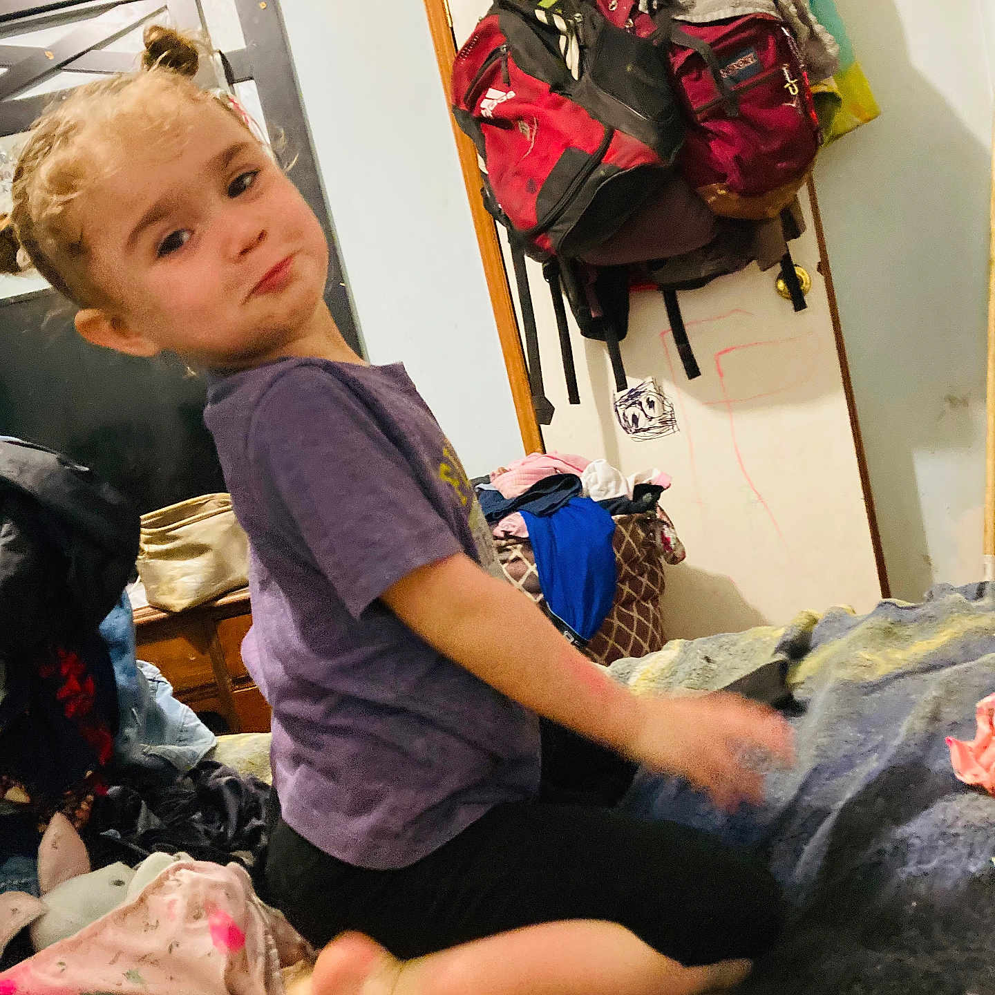 Ava joined the competition — help win amazing prizes! child, curly_hair, purple_shirt, bed, cluttered_room, backpacks, door, clothes, pouty_expression, indoors, furniture, blanket, messy, person, casual_clothing, young_child, kneeling, head, face, home
