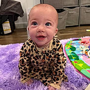 Lyla is registered to the contest to win money with this photo: baby, child, cute, eyes, face, happy, indoors, infant, leopard_print, pajamas, photography, play_mat, playroom, portrait, purple_rug, sitting, smiling, storage_bins, toys, wood_floor