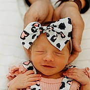 Lyla is registered to the contest to win money with this photo: newborn, baby, infant, headband, bow, hands, pink_clothing, patterned, sleeping, smile, closeup, face, cute, soft_light, portrait, peaceful, child, newborn_baby, toddler, baby_girl