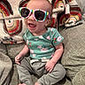 Lyla is registered to the contest to win money with this photo: baby, sunglasses, smiling, green_shirt, floral_pattern, couch, blanket, rainbow_pattern, indoor, happy, infant, cute, cozy, seated, clothing, barefoot, person, portrait, home, casual