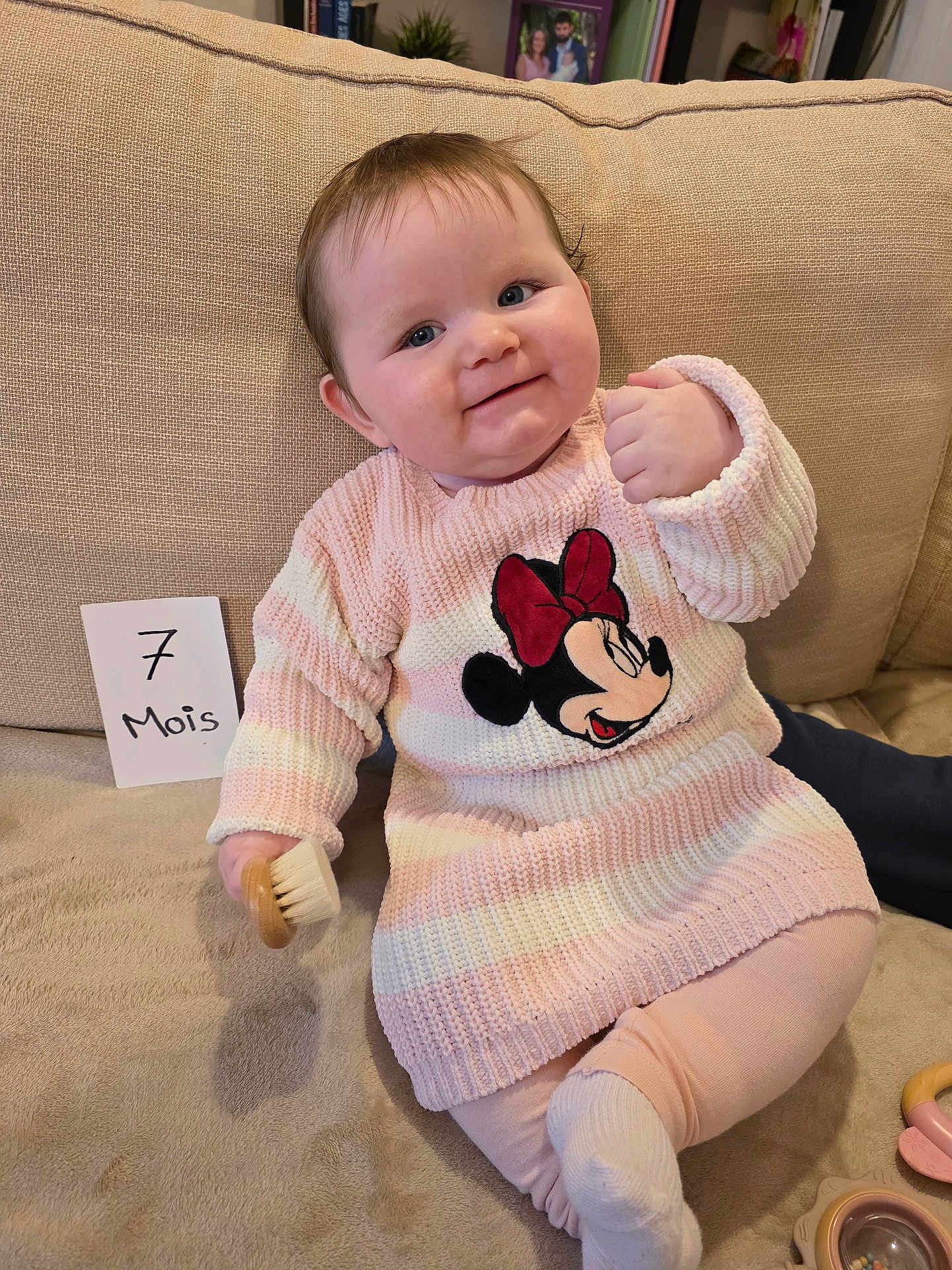 Soëlya a rejoint le concours — aidez-le/la à gagner de superbes lots ! baby, infant, child, smile, muscled_cheek, sofa, couch, blanket, card, milestone_card, brush, toy, minnie_mouse, sweater, pink_clothing, indoor, portrait, happy, hand, leg