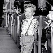 Giovanni a rejoint le concours — aidez-le/la à gagner de superbes lots ! child, boy, vintage_clothing, suspenders, bow_tie, flat_cap, church, pew, aisle, flower_decorations, black_and_white, formal_event, leaning, casual_pose, smiling, shoes, floor, people, background, portrait