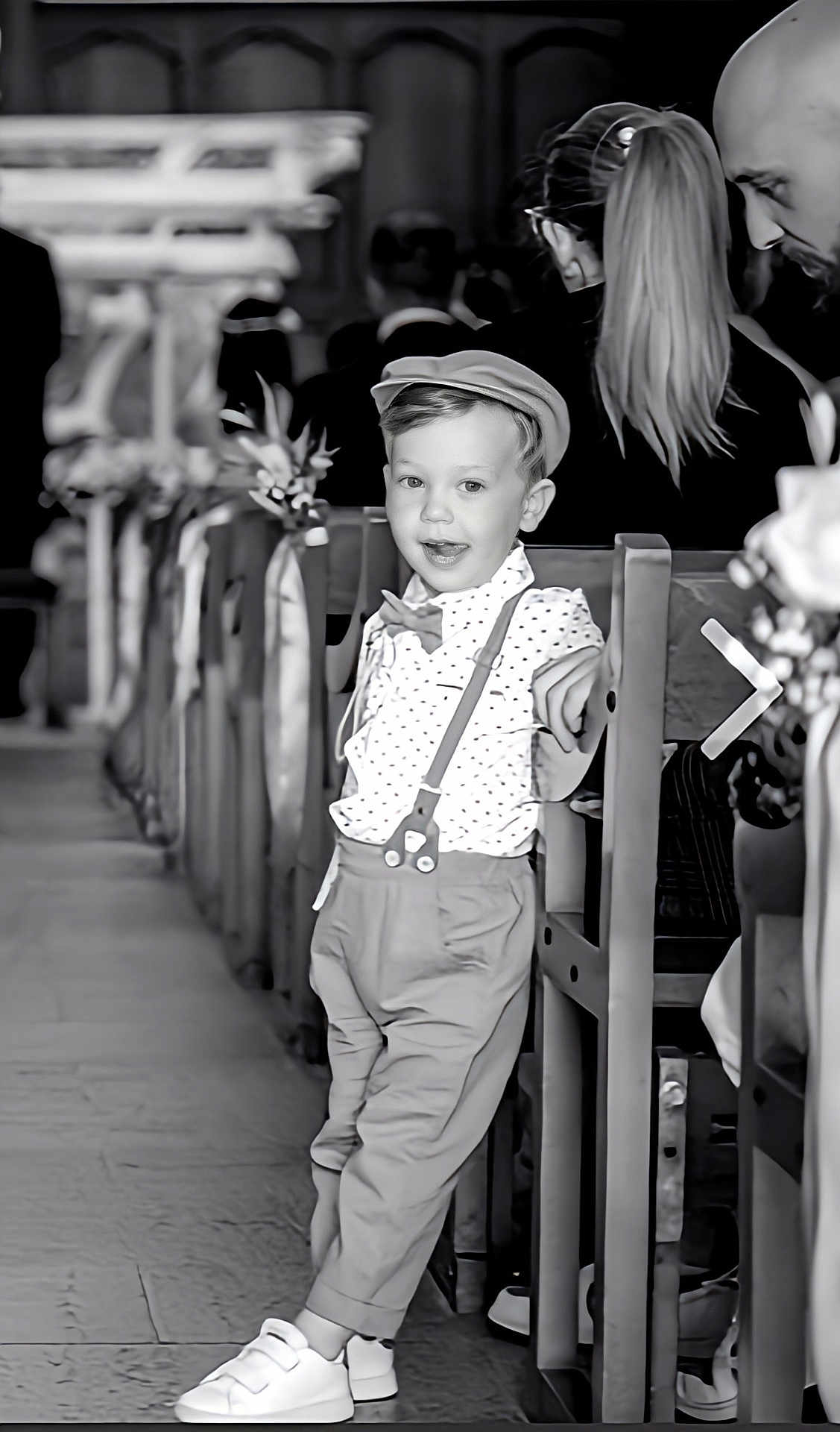 Giovanni a rejoint le concours — aidez-le/la à gagner de superbes lots ! child, boy, vintage_clothing, suspenders, bow_tie, flat_cap, church, pew, aisle, flower_decorations, black_and_white, formal_event, leaning, casual_pose, smiling, shoes, floor, people, background, portrait