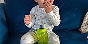 Bentley is registered to the contest to win money with this photo: baby, child, pajamas, duck_pattern, blue_couch, sippy_cup, indoor, kitchen, furniture, smiling, happy, person, sitting, face, hand, footwear, candid, home, cozy, cute