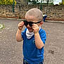 Erdem is registered to the contest to win money with this photo: child, boy, sunglasses, blue_shirt, dinosaur_pants, outdoor, playground, brick_wall, pavement, short_hair, person, casual_clothing, daylight, fun, cute, smiling, kids_playing, street, headwear, accessory