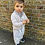 Erdem is registered to the contest to win money with this photo: child, toddler, boy, brick_wall, pavement, outdoor, clothing, sweater, pants, shoes, bandana, face, expression, curious, standing, hands, leaf, urban, casual, daylight