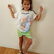Théssa participe au concours pour gagner de l'argent avec cette photo : child, girl, smiling, standing, posing, indoor, white_wall, green_shorts, graphic_tshirt, sandals, wooden_floor, happy, casual_clothing, portrait, person, fashion, cute, playful, young, feet