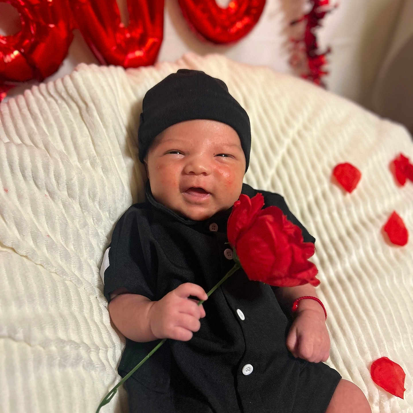 Amani joined the competition — help win amazing prizes! baby, smile, red_rose, black_clothing, beanie, white_blanket, rose_petals, balloons, love, celebration, portrait, infant, happy, cute, indoor, closeup, skin, hand, sitting, decor