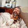 man, dog, cat, couch, living_room, relaxing, beard, white_cat, brown_dog, fur, pet, indoor, casual, resting, playful, home, furniture, person, animal, cozy