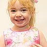 child, girl, smiling, blonde_hair, pink_dress, floral_pattern, portrait, happy, face, eyes, hair_ribbon, young, cute, person, indoors, childhood, joy, fashion, skin, expression