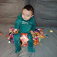 Ayden a rejoint le concours — aidez-le/la à gagner de superbes lots ! baby, candy, child, colorful, couch, curious, face, footed_pajamas, green_onesie, hand, happy, home, indoor, person, sitting, smiling, soft_furniture, toy, wrapper, young_child