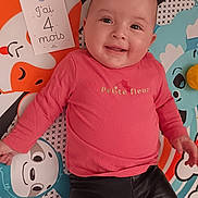 Hyuna a rejoint le concours — aidez-le/la à gagner de superbes lots ! baby, infant, smiling, playmat, milestone_card, french_text, pink_shirt, black_pants, face, eyes, tongue, toy, colorful, pattern, mat, portrait, laying, happy, closeup, baby_girl