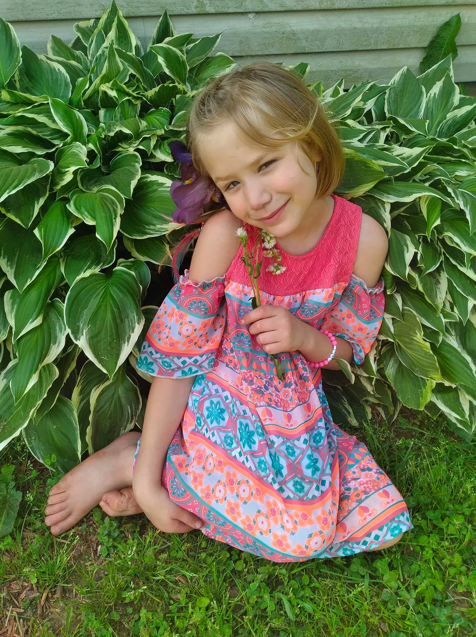 Katherine is registered to the contest to win money with this photo: baby_toddler_clothing, botany, child, day_dress, dress, grass, groundcover, happy, joy, leaf, pattern, people_in_nature, person, plant, shrub, sitting, skin, sleeve, smile, terrestrial_plant