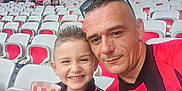 Myliano participe au concours pour gagner de l'argent avec cette photo : child, man, stadium, sports_jersey, seats, crowd, smile, glasses, fan, spectators, red, black, cup, short_hair, daylight, outdoor, happy, people, event, family