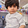 child, boy, shopping_cart, white_shirt, curly_hair, portrait, indoor, store, aisle, hand, expression, young, casual_clothing, retail, gaze, people, focus, lifestyle, cute, person