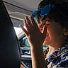 blue_sunglasses, candid, car_interior, casual_clothing, child, daylight, hand, happy, patterned_shirt, person, playful, portrait, seat, seat_back, side_view, smiling, sunlight, travel, window, young_child