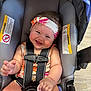 baby, car_seat, child, clothing, eyes, face, floor, hand, happy, headband, indoor, infant, mouth, pacifier, seat_belt, security, sitting, skin, smile, straps