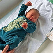 Aaron participe au concours pour gagner de l'argent avec cette photo : baby, infant, sleeping, onesie, dinosaur, blue_clothing, hand, towel, changing_table, newborn, person, cute, indoor, child, skin, face, fingers, foot, sleep, resting