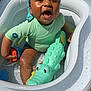 bandana, child, crocodile_toy, face, fun, happy, inflatable_pool, outdoor, person, playing, pool, sitting, skin, smiling, summer, sunlight, swim_shirt, toddler, toy, water