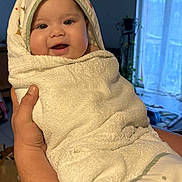 Arya participe au concours pour gagner de l'argent avec cette photo : baby, infant, towel, wrapped, smiling, face, hand, indoors, window, curtains, plant, cozy, cute, child, person, blanket, soft, hooded_towel, home, happy