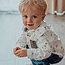 toddler, child, blonde_hair, blue_eyes, white_shirt, animal_print, denim_jeans, socks, wooden_floor, indoor, crouching, smiling, curious, portrait, casual_clothing, cute, young_child, natural_light, home, person