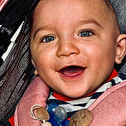 Julio participe au concours pour gagner de l'argent avec cette photo : baby, smiling, blue_eyes, pacifier, harness, striped_clothing, close_up, happy, infant, cute, child, face, mouth_open, pink, wooden_beads, cheerful, portrait, person, seat, accessory