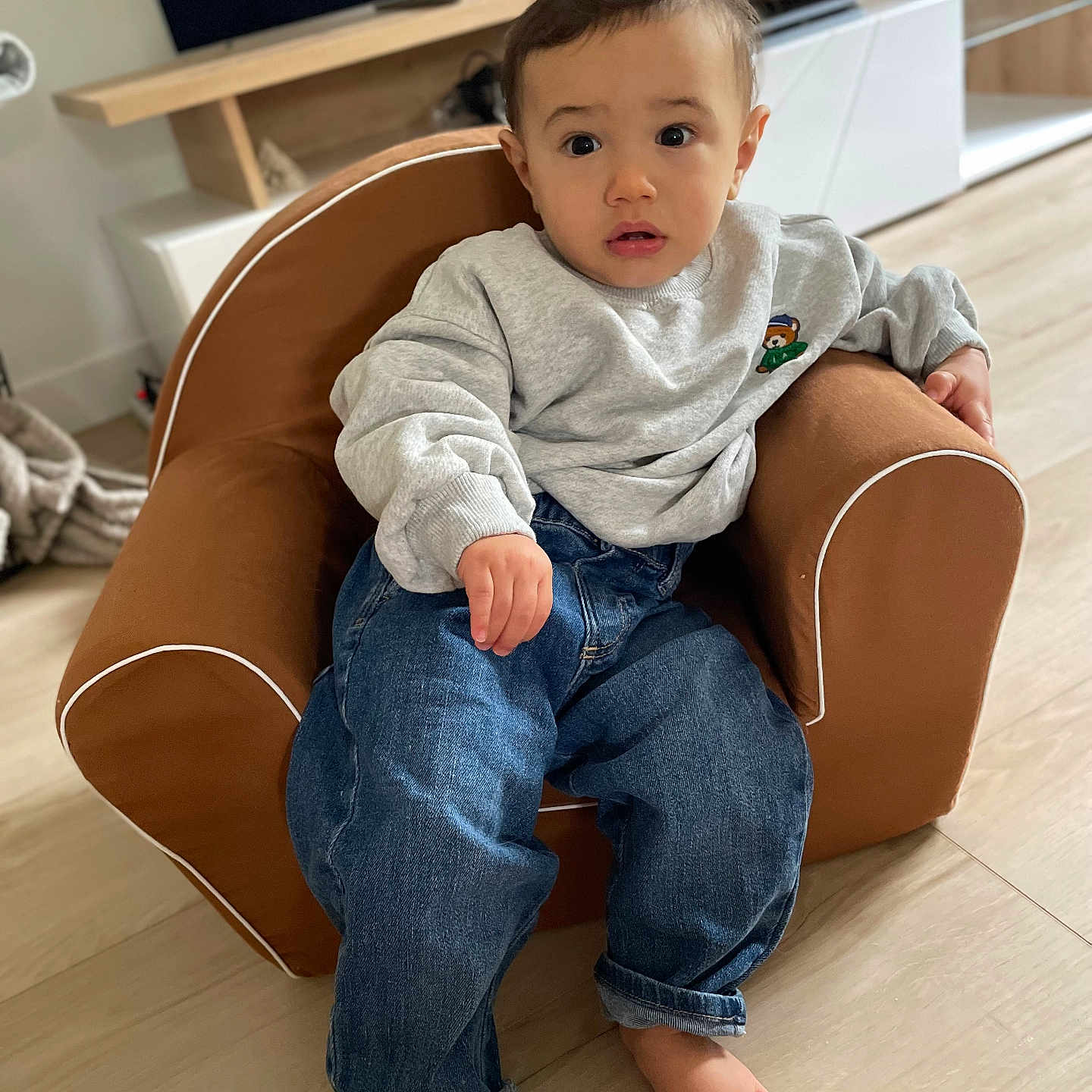 Sacha Leroux a rejoint le concours — aidez-le/la à gagner de superbes lots ! armchair, barefoot, casual_wear, child, clothing, curious, cute, expression, floor, furniture, home, indoor, jeans, living_room, person, relaxed, seated, sweatshirt, toddler, young_child