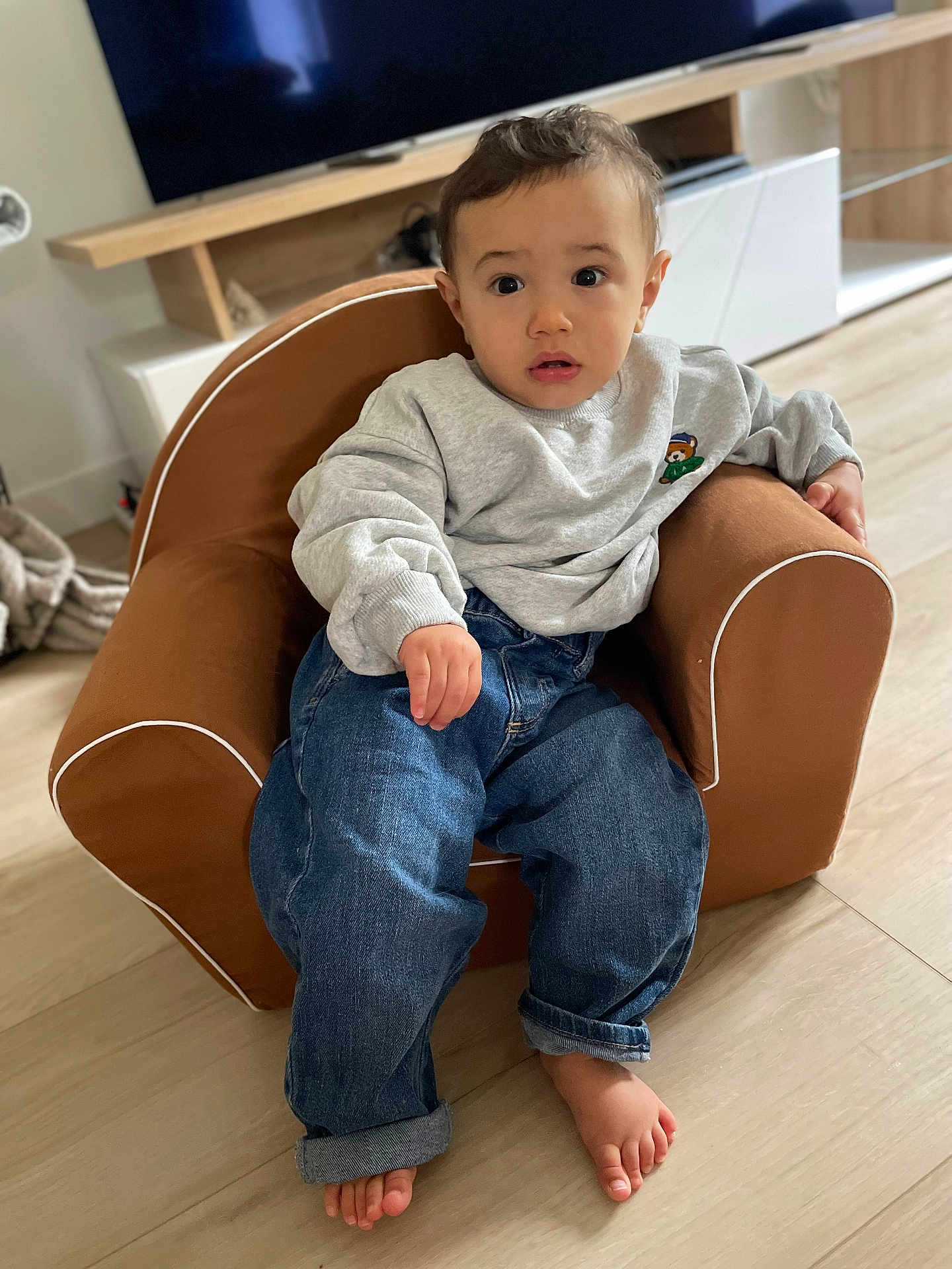 Sacha Leroux a rejoint le concours — aidez-le/la à gagner de superbes lots ! armchair, barefoot, casual_wear, child, clothing, curious, cute, expression, floor, furniture, home, indoor, jeans, living_room, person, relaxed, seated, sweatshirt, toddler, young_child