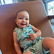 Stefano is registered to the contest to win money with this photo: baby, smiling, child, romper, floral_pattern, chair, indoor, natural_light, happy, cute, skin, arm, leg, bracelet, window, modern_furniture, casual, portrait, infant, relaxed