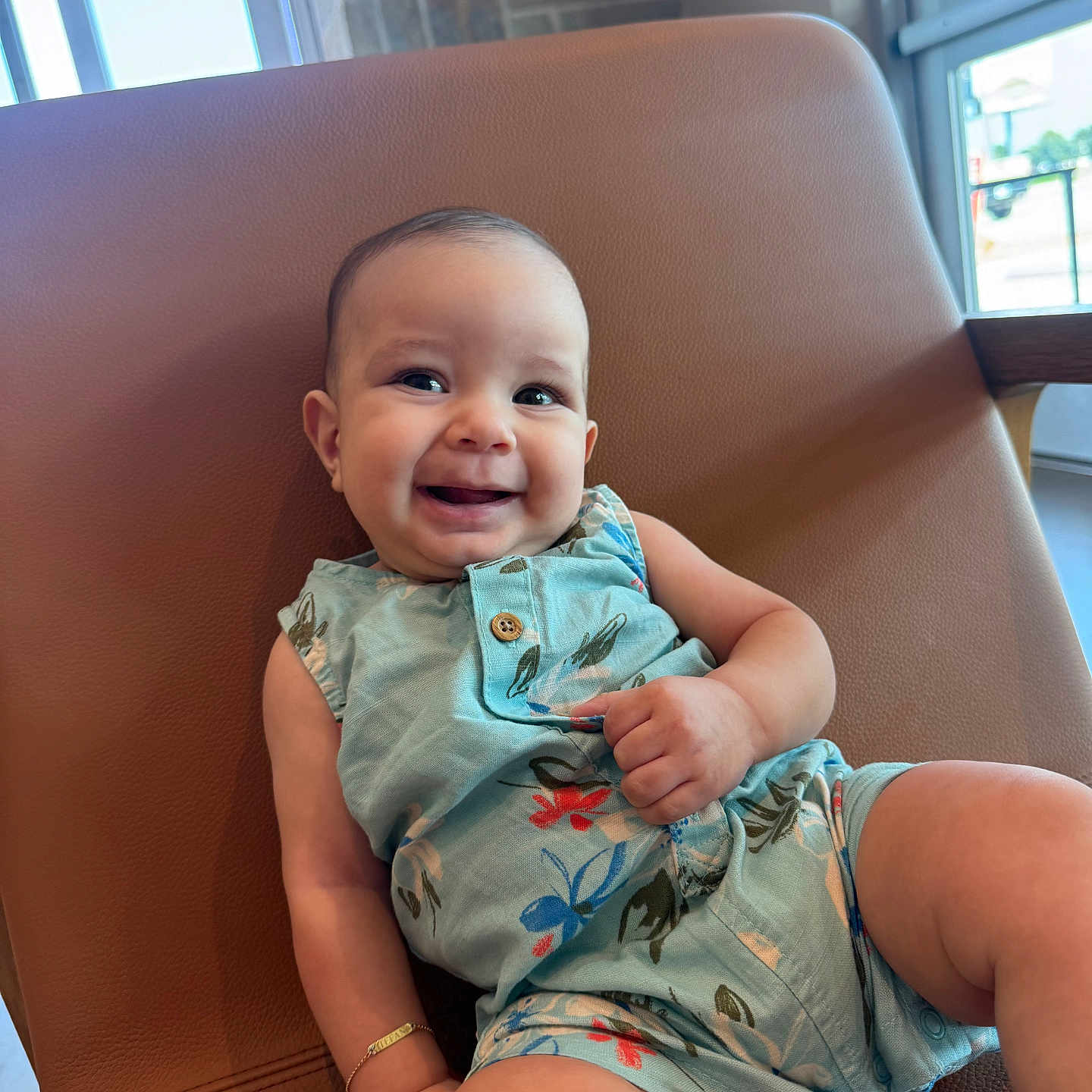 Stefano is registered to the contest to win money with this photo: arm, baby, bracelet, casual, chair, child, cute, floral_pattern, happy, indoor, infant, leg, modern_furniture, natural_light, portrait, relaxed, romper, skin, smiling, window