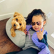 Rico is registered to the contest to win money with this photo: casual_clothing, child, cozy, curly_hair, dog, gray_bed, hand_sign, happy, indoor, light_wall, outlet, pet, playful, portrait, purple_vest, reflection, relaxed, smiling, sunglasses, wooden_floor