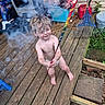 toddler, child, sparkler, smoke, wooden_deck, outdoor, barefoot, summer, happy, toy, play, backyard, garden_tools, gas_can, rake, diaper, person, curly_hair, daylight, celebration