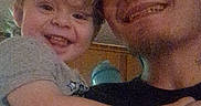 Waylon is registered to the contest to win money with this photo: toddler, child, smiling, male, person, curly_hair, indoor, casual, holding, happy, young_adult, face, headwear, arm, embrace, family, portrait, clothing, people, affection