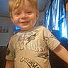 child, toddler, smiling, blonde_hair, tshirt, hot_wheels, indoor, window, curtains, daylight, person, happy, portrait, casual, clothing, young_child, face, standing, home, interior