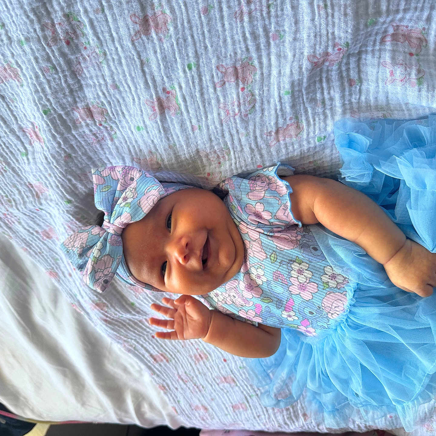 Madisson Zevallos joined the competition — help win amazing prizes! baby, bed, blanket, blue_dress, child, clothing, cute, face, hand, happy, headband, indoors, infant, lying_down, patterned_blanket, portrait, smiling, soft_texture, toddler, tutu