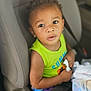child, toddler, car_seat, seat_belt, green_shirt, colorful_shorts, plastic_bag, curly_hair, indoor, car_interior, safety, seat, person, cute, young, baby, expression, holding, travel, looking_up