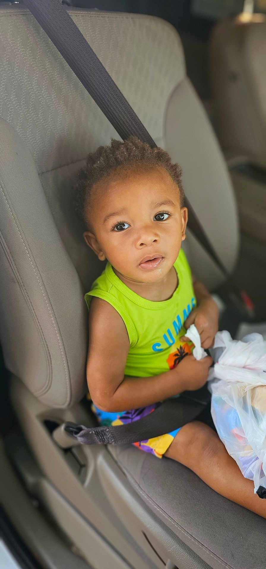 Kymere joined the competition — help win amazing prizes! child, toddler, car_seat, seat_belt, green_shirt, colorful_shorts, plastic_bag, curly_hair, indoor, car_interior, safety, seat, person, cute, young, baby, expression, holding, travel, looking_up