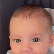Griselda is registered to the contest to win money with this photo: baby, child, face, smile, drool, grey_clothing, cute, portrait, infant, head, eyes, earring, skin, sitting, indoors, young_child, cushion, soft_light, closeup, happy
