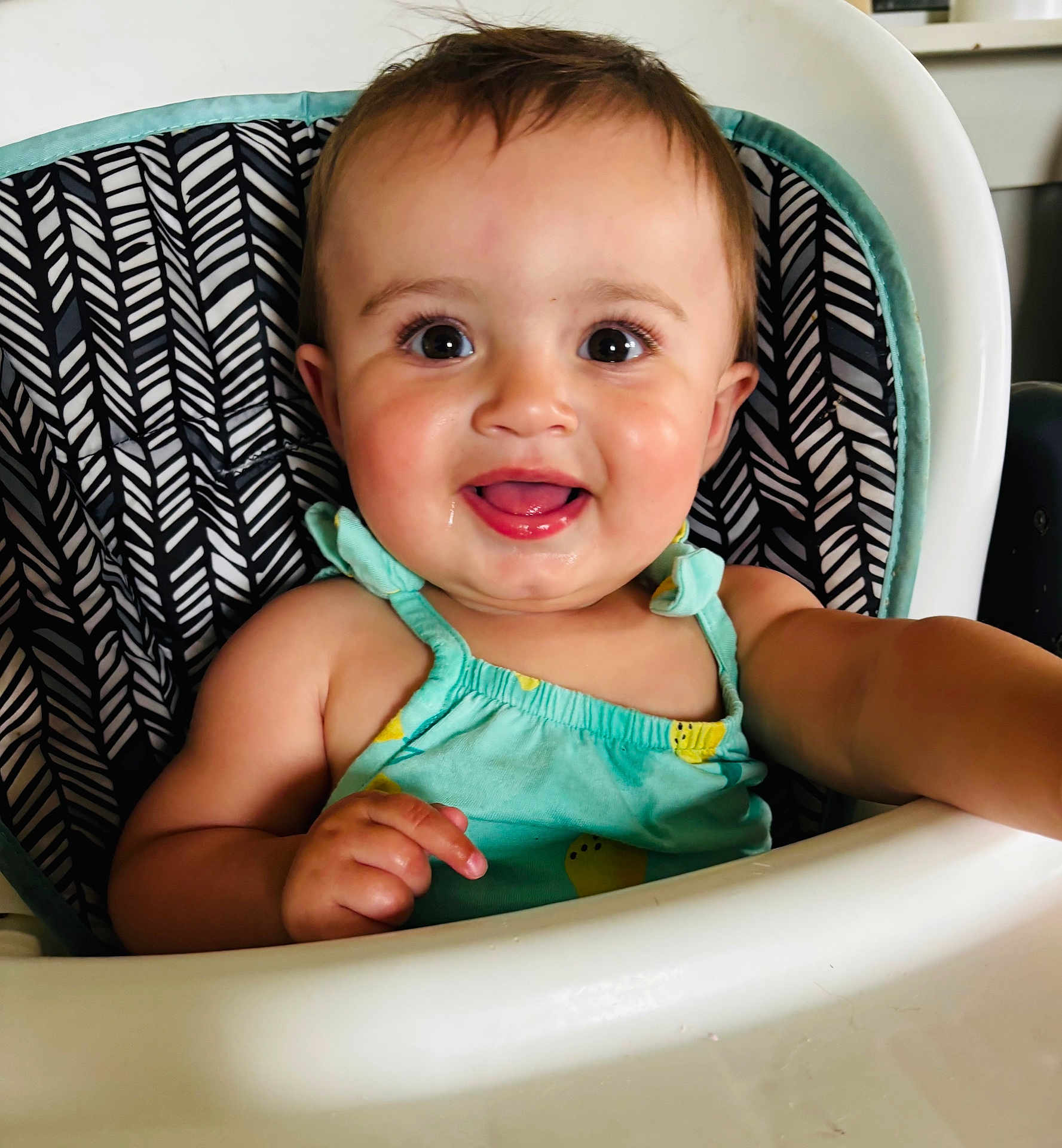 Ariella joined the competition — help win amazing prizes! baby, child, high_chair, smiling, happy, face, person, clothing, sitting, indoor, cute, portrait, young_child, infant, dressed, seat, furniture, skin, head, arm