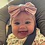 baby, smiling, headband, pink_bow, car_seat, safety_strap, floral_dress, happy, infant, face, child, cute, closeup, person, indoors, seat, baby_clothes, portrait, cheerful, young_child