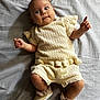 baby, infant, knitted_clothing, cream_color, lying_down, blanket, footwear, booties, socks, curious_expression, portrait, indoors, soft_lighting, cute, child, human, small_hands, small_feet, fabric_texture, cozy
