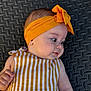 adorable, baby, cheeks, child, closeup, curious, cute, dress, face, hand, headband, indoors, infant, lying_down, portrait, skin, soft_light, striped_dress, textured_background, yellow